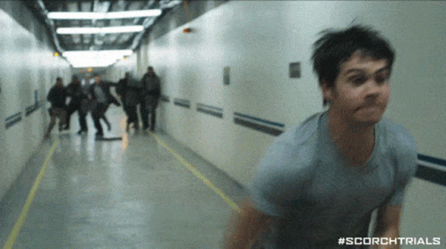 A Man In A Blue Shirt Is Running Down A Hallway With #Scorchtrials On The Bottom GIF