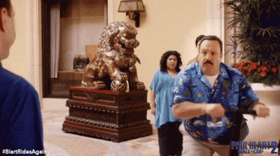 A Man In A Blue Shirt Is Running In Front Of A Statue Of A Lion .. GIF