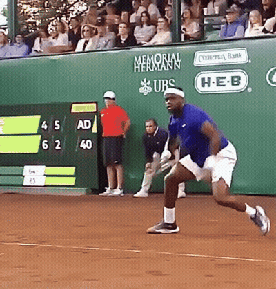 A Man In A Blue Shirt Is Running On A Tennis Court In Front Of A Memorial Hermann Banner GIF