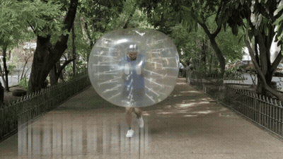 A Man In A Blue Shirt Is Running Through A Clear Bubble On A Sidewalk GIF