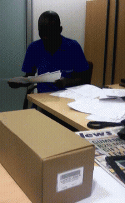 A Man In A Blue Shirt Is Sitting At A Desk With A Box That Says News GIF