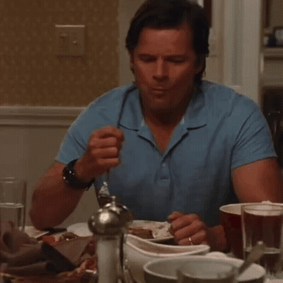 A Man In A Blue Shirt Is Sitting At A Table Eating Something GIF