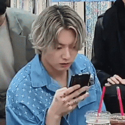 A Man In A Blue Shirt Is Sitting At A Table Looking At His Phone . GIF