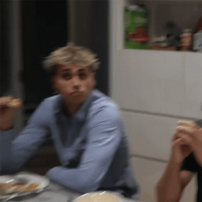 A Man In A Blue Shirt Is Sitting At A Table With A Plate Of Food . GIF