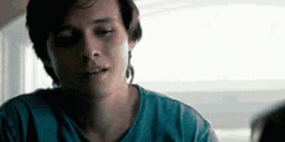 A Man In A Blue Shirt Is Sitting At A Table With His Eyes Closed And Looking At Something . GIF