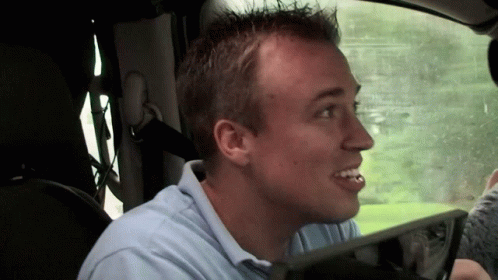A Man In A Blue Shirt Is Sitting In A Car With His Mouth Open GIF
