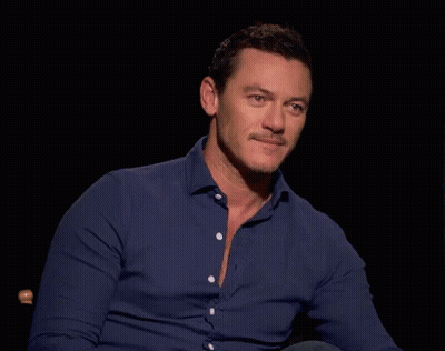 A Man In A Blue Shirt Is Sitting In A Chair In A Dark Room GIF