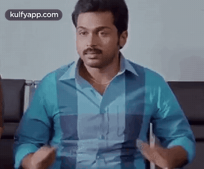 A Man In A Blue Shirt Is Sitting In A Chair Talking To Someone . GIF