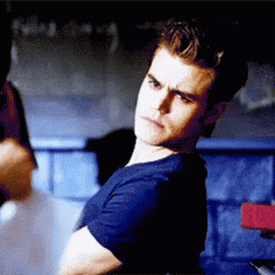 A Man In A Blue Shirt Is Sitting In A Dark Room . GIF