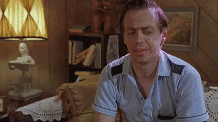 A Man In A Blue Shirt Is Sitting In A Living Room With A Lamp . GIF
