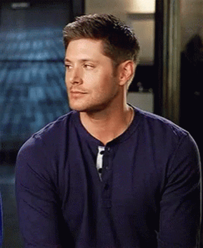 A Man In A Blue Shirt Is Sitting In A Room And Looking At The Camera . GIF