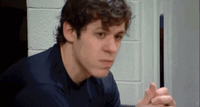 A Man In A Blue Shirt Is Sitting In A Room With His Hands Folded . GIF
