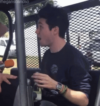 A Man In A Blue Shirt Is Sitting In A Vehicle Behind A Fence . GIF