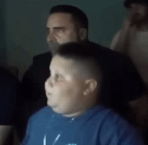 A Man In A Blue Shirt Is Sitting In Front Of A Man In A Black Suit . GIF