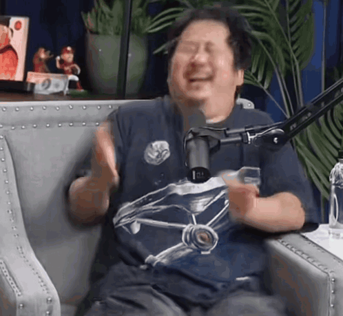 A Man In A Blue Shirt Is Sitting In Front Of A Microphone GIF
