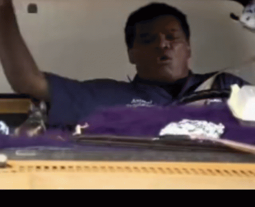 A Man In A Blue Shirt Is Sitting In Front Of A Purple And White Item GIF