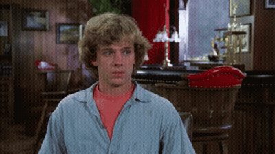 A Man In A Blue Shirt Is Sitting In Front Of A Red Chair GIF