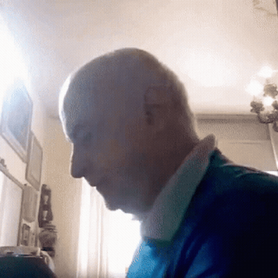 A Man In A Blue Shirt Is Sitting In Front Of A Window . GIF