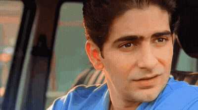 A Man In A Blue Shirt Is Sitting In The Back Seat Of A Car And Looking At The Camera . GIF