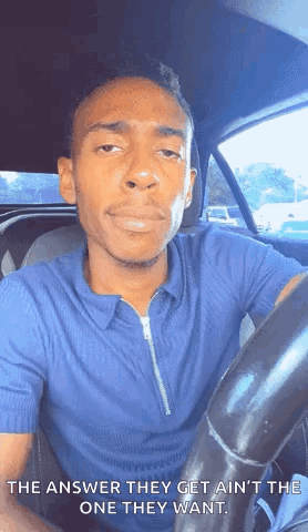 A Man In A Blue Shirt Is Sitting In The Driver 'S Seat Of A Car And Making A Face . GIF