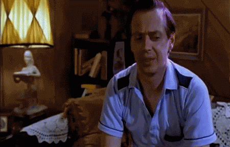 A Man In A Blue Shirt Is Sitting On A Bed In A Dark Room GIF