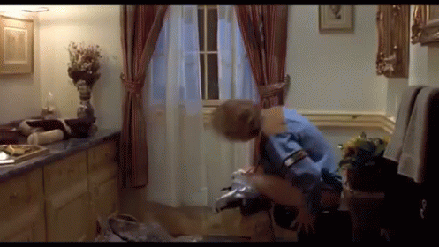 A Man In A Blue Shirt Is Sitting On A Chair In A Bathroom GIF