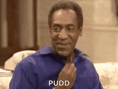 A Man In A Blue Shirt Is Sitting On A Couch And Smiling While Holding His Hand To His Chest . GIF