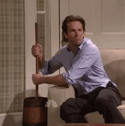 A Man In A Blue Shirt Is Sitting On A Couch Holding A Mop . GIF