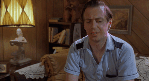 A Man In A Blue Shirt Is Sitting On A Couch In A Living Room GIF