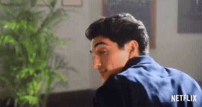 A Man In A Blue Shirt Is Sitting On A Couch In A Living Room With A Plant In The Background . GIF