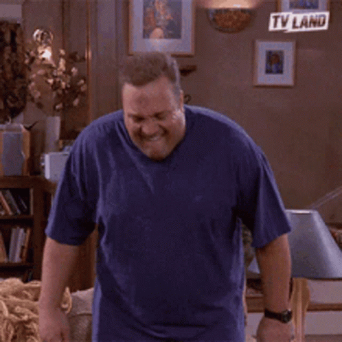 A Man In A Blue Shirt Is Sitting On A Couch In A Living Room With Tv Land Written On The Wall Behind Him GIF