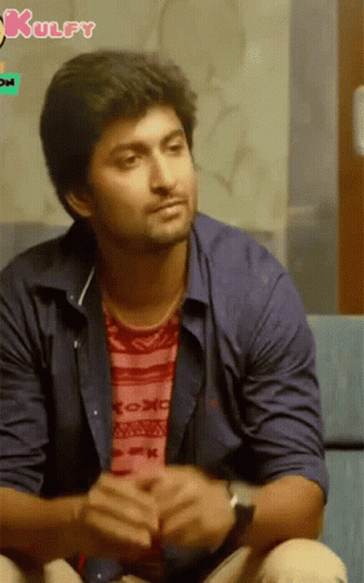 A Man In A Blue Shirt Is Sitting On A Couch With A Kulfy Logo In The Background GIF