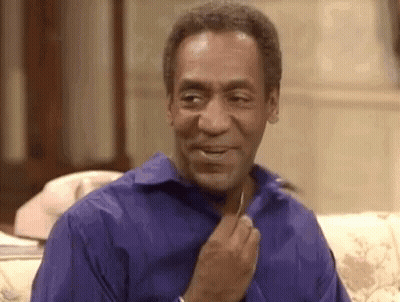 A Man In A Blue Shirt Is Sitting On A Couch With His Hand On His Chest . GIF