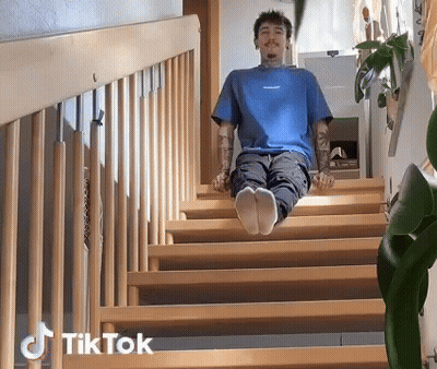 A Man In A Blue Shirt Is Sitting On A Set Of Wooden Stairs With Tiktok Written On The Bottom Right GIF