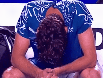 A Man In A Blue Shirt Is Sitting With His Head Down And His Hands Folded . GIF