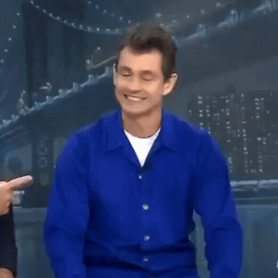 A Man In A Blue Shirt Is Smiling And Pointing At The Camera GIF
