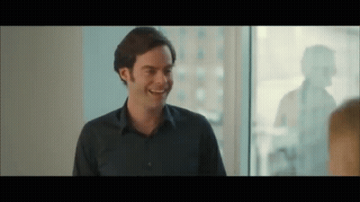 A Man In A Blue Shirt Is Smiling And Talking To Another Man In Front Of A Window . GIF