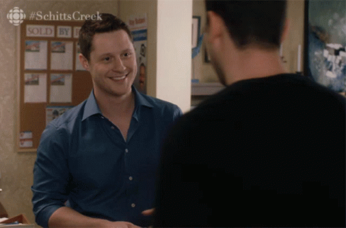 A Man In A Blue Shirt Is Smiling In Front Of A Sold By Sign GIF