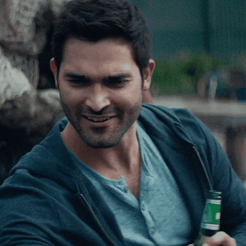 A Man In A Blue Shirt Is Smiling While Holding A Bottle GIF