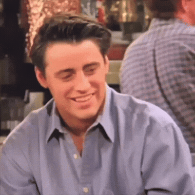 A Man In A Blue Shirt Is Smiling While Sitting In A Bar . GIF