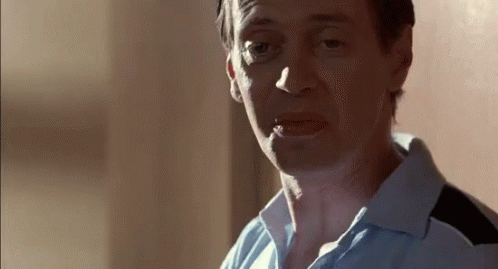 A Man In A Blue Shirt Is Smoking A Cigarette While Looking At The Camera . GIF