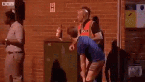 A Man In A Blue Shirt Is Squatting Down In Front Of A Brick Wall . GIF