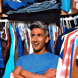 A Man In A Blue Shirt Is Standing In A Closet Full Of Clothes GIF