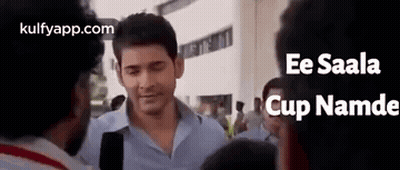 A Man In A Blue Shirt Is Standing In A Crowd Of People . GIF