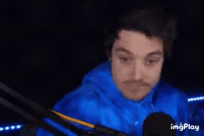 A Man In A Blue Shirt Is Standing In A Dark Room With His Hands Behind His Back . GIF
