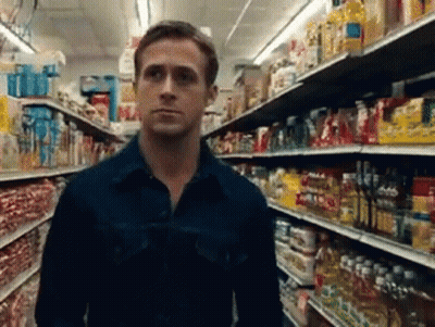 A Man In A Blue Shirt Is Standing In A Grocery Store Aisle Looking At Something GIF