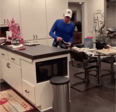 A Man In A Blue Shirt Is Standing In A Kitchen Holding A Shirt That Says Limit GIF