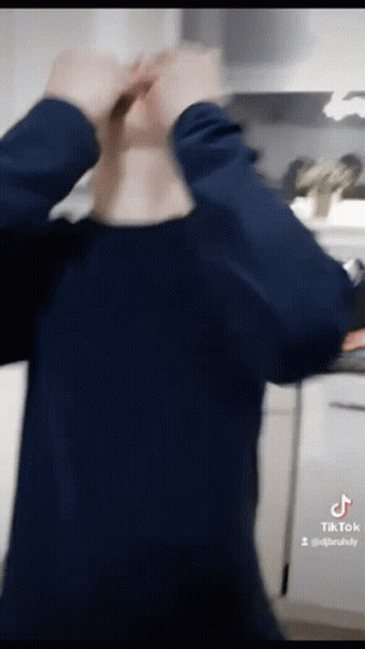 A Man In A Blue Shirt Is Standing In A Kitchen With His Hands On His Head GIF