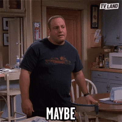 A Man In A Blue Shirt Is Standing In A Kitchen With The Word Maybe On His Shirt . GIF