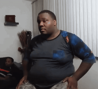 A Man In A Blue Shirt Is Standing In A Living Room . GIF